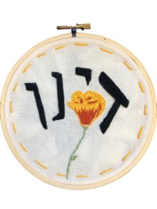 an embroidered California poppy with the Hebrew word “Dayenu” stitched above 